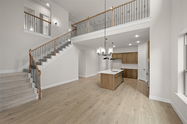 kitchen with brown cabinets, a kitchen island with sink, light wood-style floors, light countertops, and a chandelier