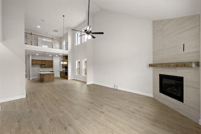 unfurnished living room with a tiled fireplace, baseboards, light wood-type flooring, and ceiling fan