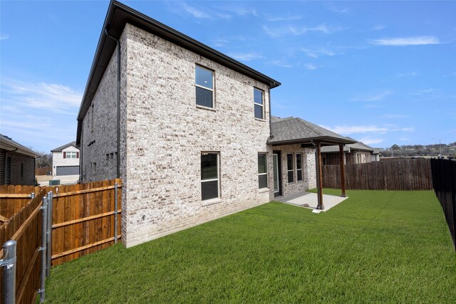 back of property with a yard, a patio, brick siding, and a fenced backyard