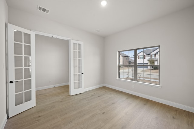 empty room featuring french doors, visible vents, light wood finished floors, and baseboards