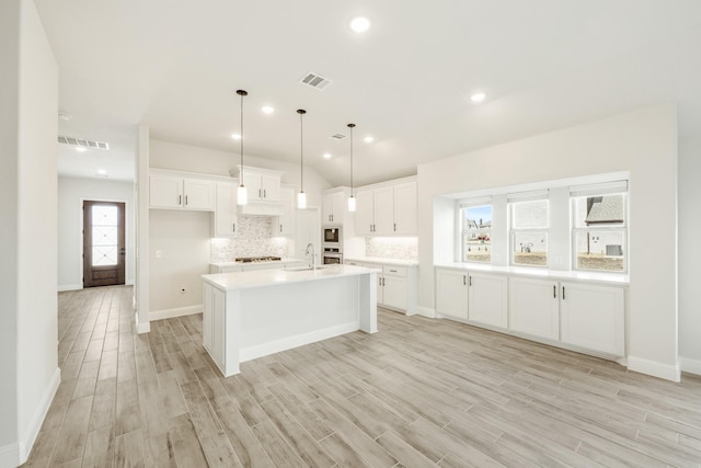 kitchen featuring sink, a kitchen island with sink, light hardwood / wood-style floors, white cabinets, and decorative backsplash