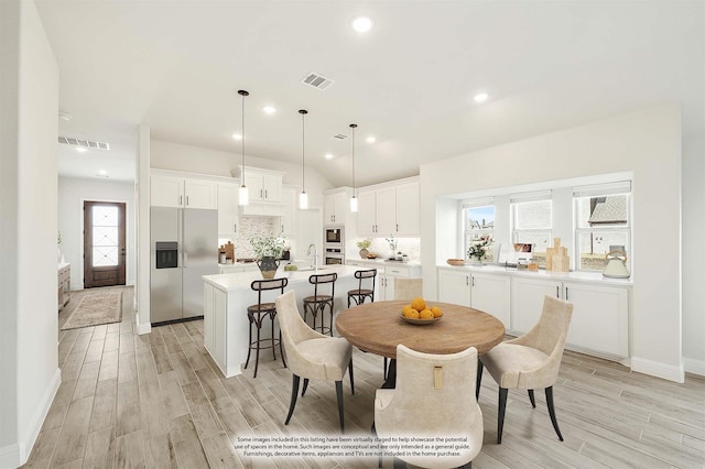 dining space with vaulted ceiling, sink, and light hardwood / wood-style flooring