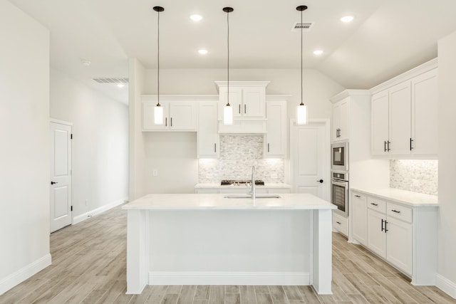 kitchen featuring hanging light fixtures, white cabinetry, appliances with stainless steel finishes, and a center island with sink