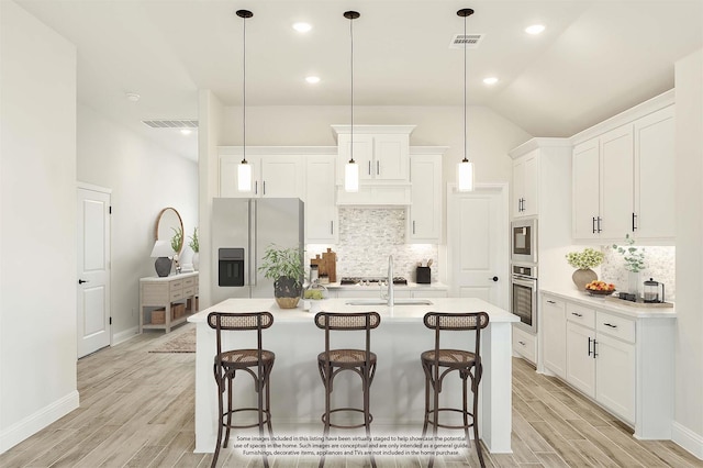 kitchen with stainless steel appliances, decorative light fixtures, an island with sink, and white cabinets