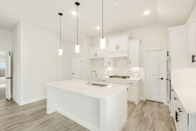 kitchen with a kitchen island with sink, sink, hanging light fixtures, and white cabinets