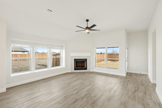 unfurnished living room featuring a tile fireplace, plenty of natural light, ceiling fan, and light hardwood / wood-style floors