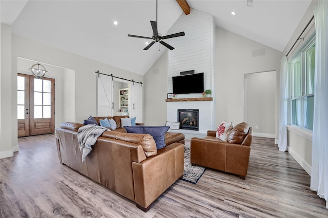 living room featuring a barn door, a fireplace, wood finished floors, and beam ceiling