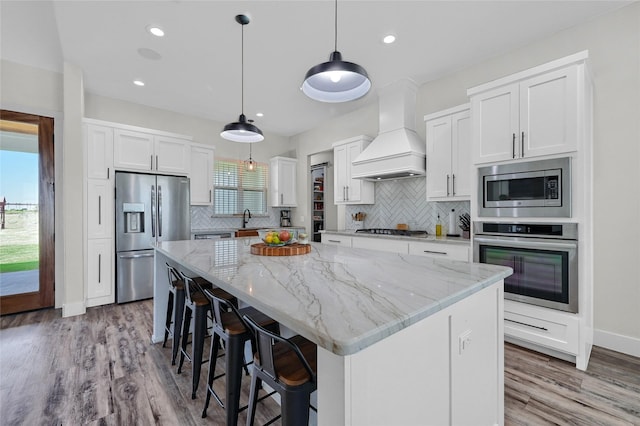 kitchen featuring a center island, a breakfast bar, custom exhaust hood, stainless steel appliances, and white cabinets