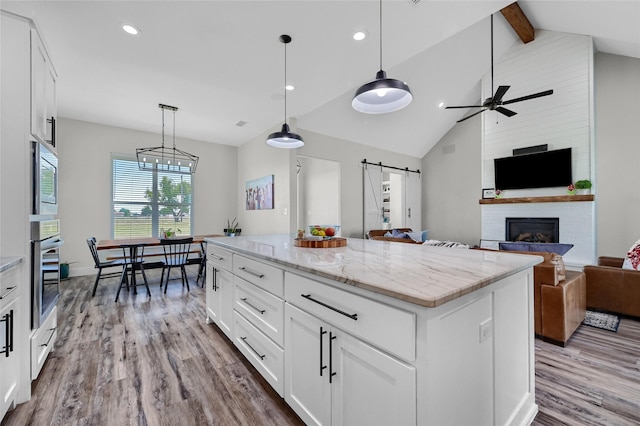 kitchen with a barn door, open floor plan, wood finished floors, beamed ceiling, and stainless steel appliances