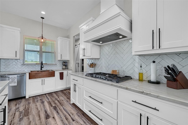 kitchen with white cabinets, wood finished floors, custom exhaust hood, stainless steel appliances, and a sink