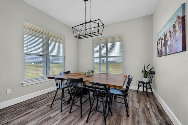 dining room with dark wood-type flooring, a notable chandelier, and baseboards