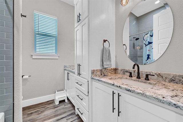 full bathroom with wood finished floors, a tile shower, vanity, and baseboards