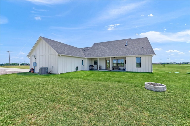 back of house featuring roof with shingles, a lawn, board and batten siding, central AC, and a fire pit