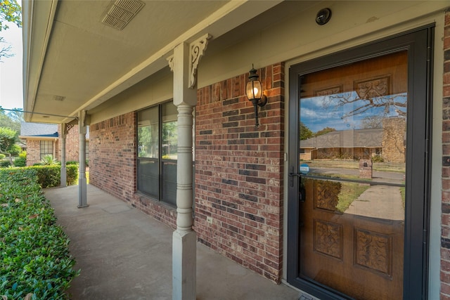 entrance to property featuring covered porch, brick siding, and visible vents