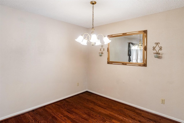 empty room with a notable chandelier, baseboards, and wood finished floors