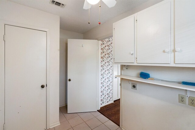 interior space featuring ceiling fan, light wood-type flooring, electric dryer hookup, cabinets, and a textured ceiling