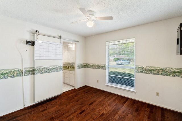 spare room featuring hardwood / wood-style floors, a barn door, a textured ceiling, and ceiling fan