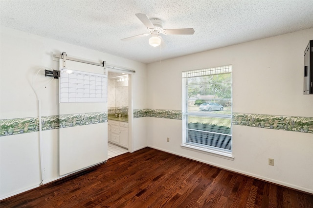 unfurnished room featuring a textured ceiling, ceiling fan, a barn door, and wood finished floors