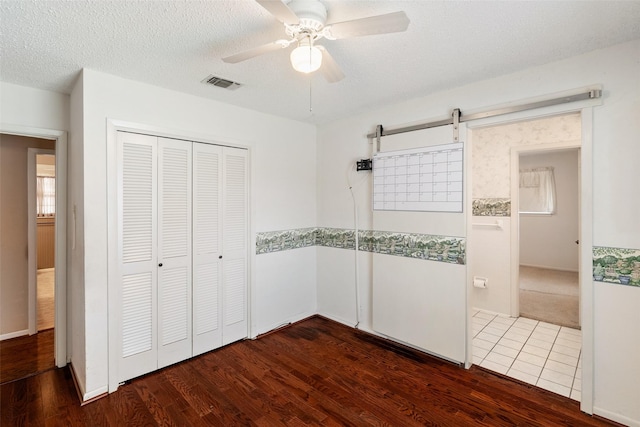 unfurnished bedroom with dark wood finished floors, a closet, visible vents, ceiling fan, and a textured ceiling