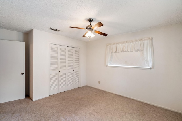 unfurnished bedroom featuring a textured ceiling, ceiling fan, carpet floors, visible vents, and a closet