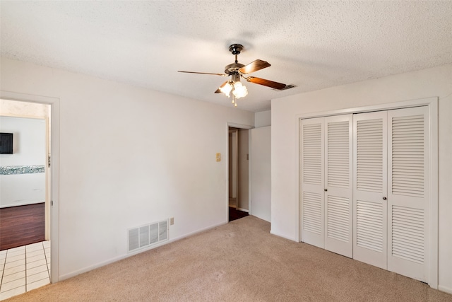 unfurnished bedroom featuring ceiling fan, light carpet, a closet, and a textured ceiling