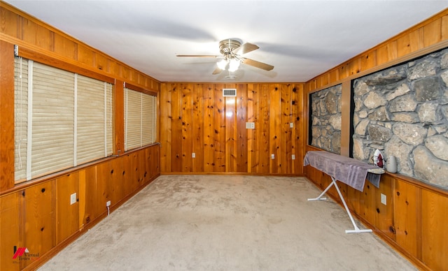 carpeted spare room with wood walls and ceiling fan