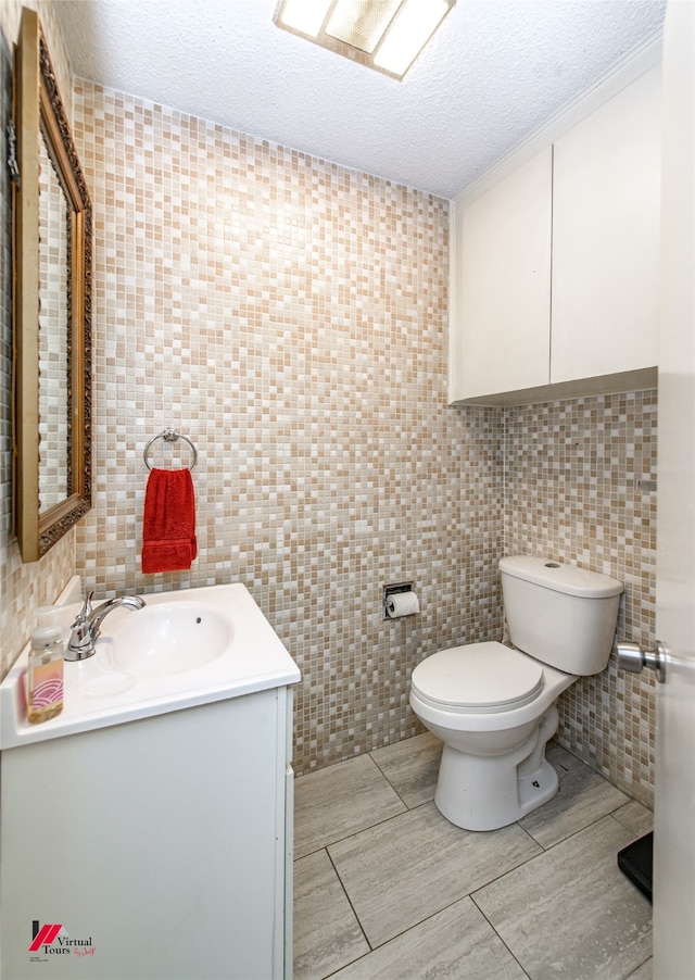 bathroom featuring tile walls, a textured ceiling, vanity, and toilet