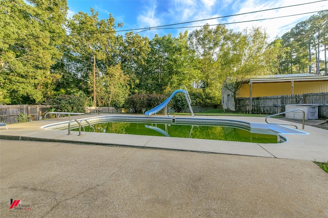 view of pool with a water slide, central AC unit, and a diving board