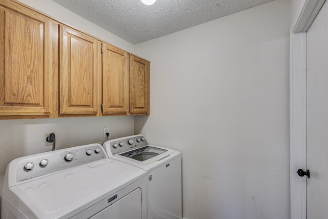 clothes washing area with a textured ceiling, cabinets, and washing machine and clothes dryer