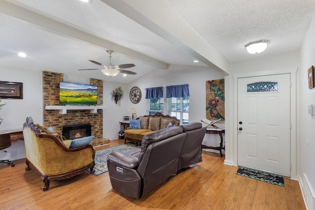 living room with a brick fireplace, light hardwood / wood-style floors, a textured ceiling, ceiling fan, and brick wall