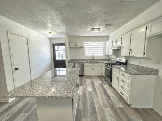 kitchen with stainless steel appliances, stone countertops, sink, and light hardwood / wood-style flooring