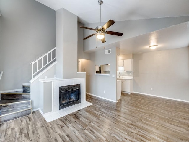 unfurnished living room featuring ceiling fan, a tile fireplace, visible vents, light wood-style floors, and stairway