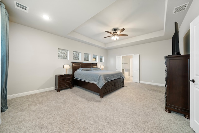 carpeted bedroom with a raised ceiling, ceiling fan, and ensuite bath