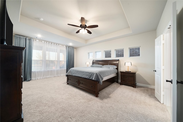 bedroom with light colored carpet, ceiling fan, and a tray ceiling