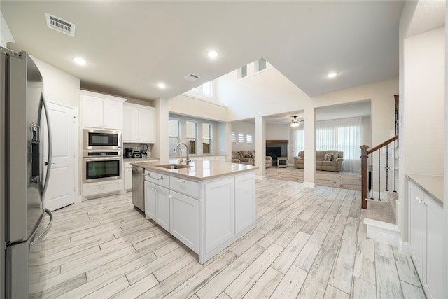 kitchen with stainless steel appliances, white cabinetry, sink, ceiling fan, and a kitchen island with sink