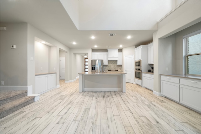 kitchen with backsplash, light wood-type flooring, stainless steel appliances, white cabinetry, and an island with sink