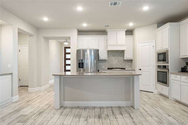 kitchen featuring light wood-type flooring, white cabinets, stainless steel appliances, and an island with sink