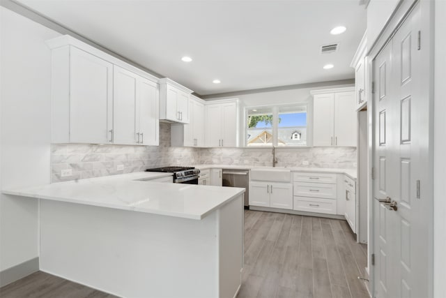 kitchen featuring appliances with stainless steel finishes, kitchen peninsula, white cabinetry, and light hardwood / wood-style flooring