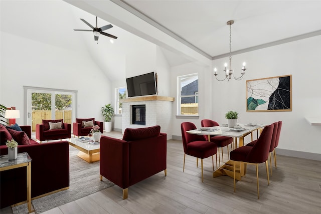 dining room featuring ceiling fan with notable chandelier, light wood-type flooring, a fireplace, and high vaulted ceiling