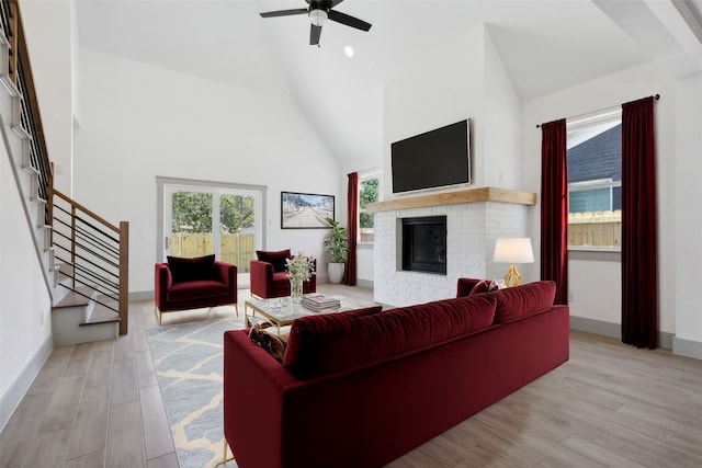 living room featuring high vaulted ceiling, light wood-type flooring, ceiling fan, and a fireplace