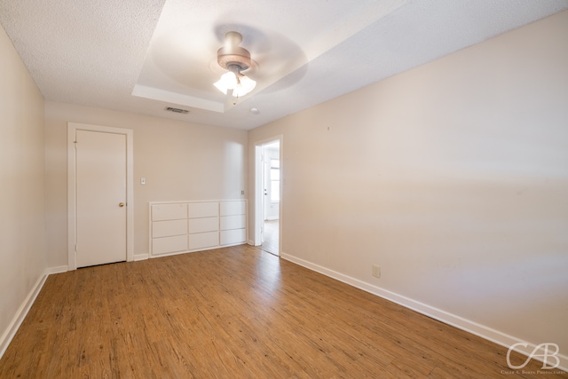 unfurnished room with a raised ceiling, wood-type flooring, a textured ceiling, and ceiling fan