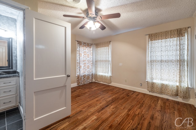 empty room with a healthy amount of sunlight, ceiling fan, dark wood-type flooring, and a textured ceiling