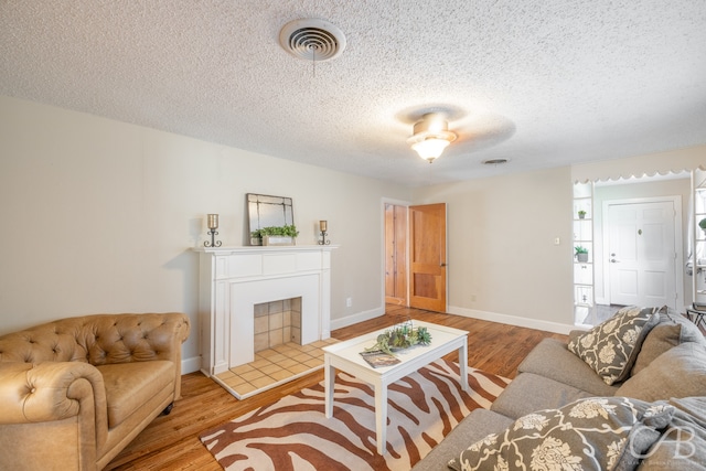 living room featuring a fireplace, ceiling fan, light hardwood / wood-style flooring, and a textured ceiling