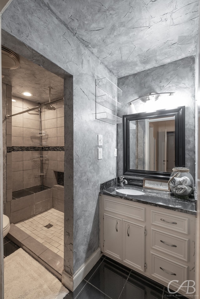 bathroom with tile patterned floors, toilet, tiled shower, and vanity