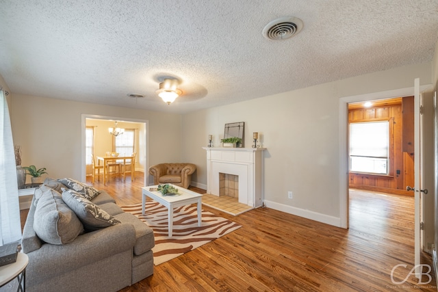 living room with a textured ceiling, an inviting chandelier, light wood-type flooring, and a tiled fireplace