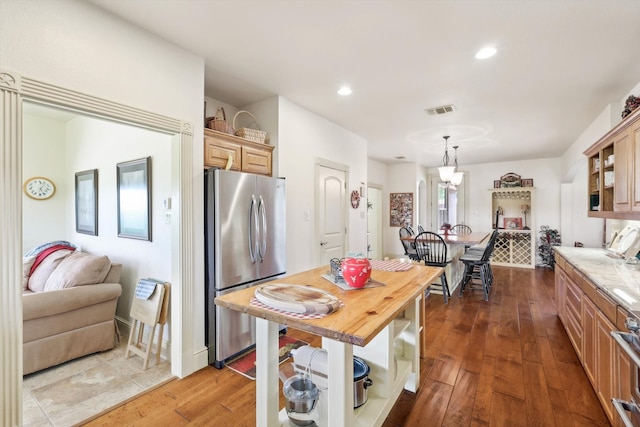 kitchen featuring light brown cabinetry, hanging light fixtures, stainless steel refrigerator, butcher block counters, and hardwood / wood-style flooring