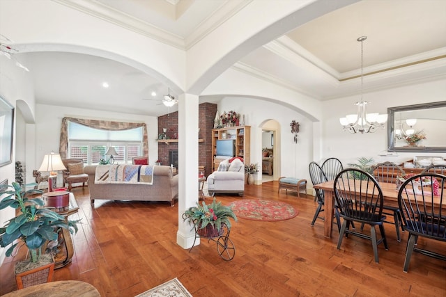 dining room with brick wall, a fireplace, ceiling fan with notable chandelier, a tray ceiling, and hardwood / wood-style flooring