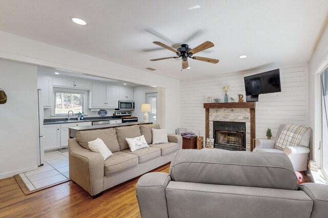 living room with ceiling fan, a stone fireplace, and hardwood / wood-style floors