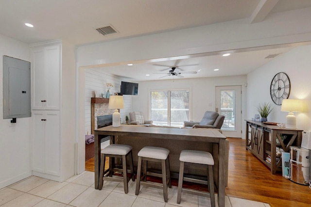 dining area with light hardwood / wood-style floors, a stone fireplace, electric panel, and ceiling fan