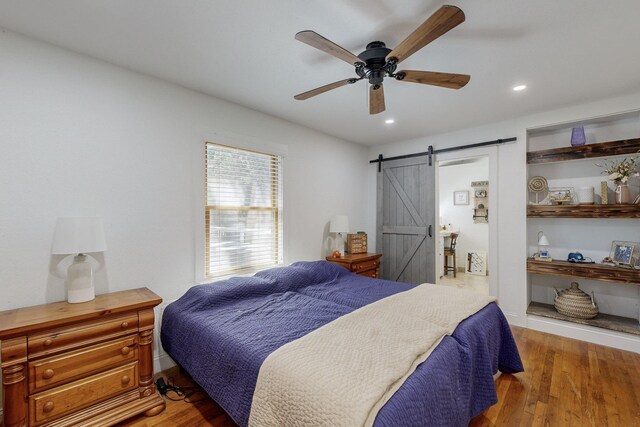 bedroom with a barn door, ceiling fan, and hardwood / wood-style flooring